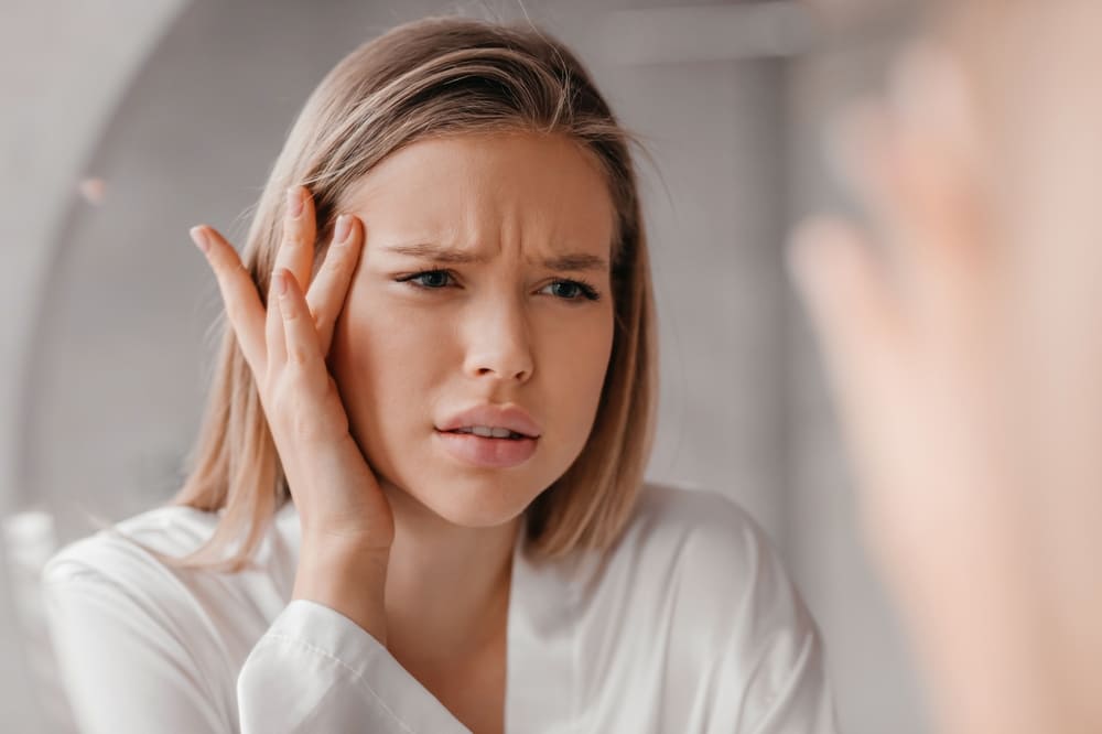 Mirror reflection of upset lady looking at mirror and touching her forehead.